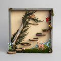 Decorative diorama with plants, figurines, and a branch on a textured surface.
