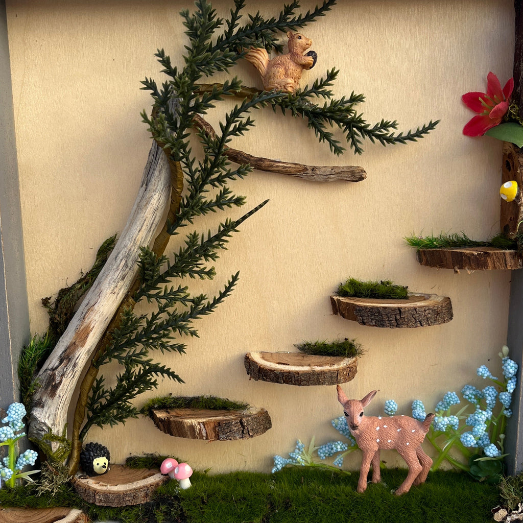 Decorative diorama with plants, figurines, and a branch on a textured surface.