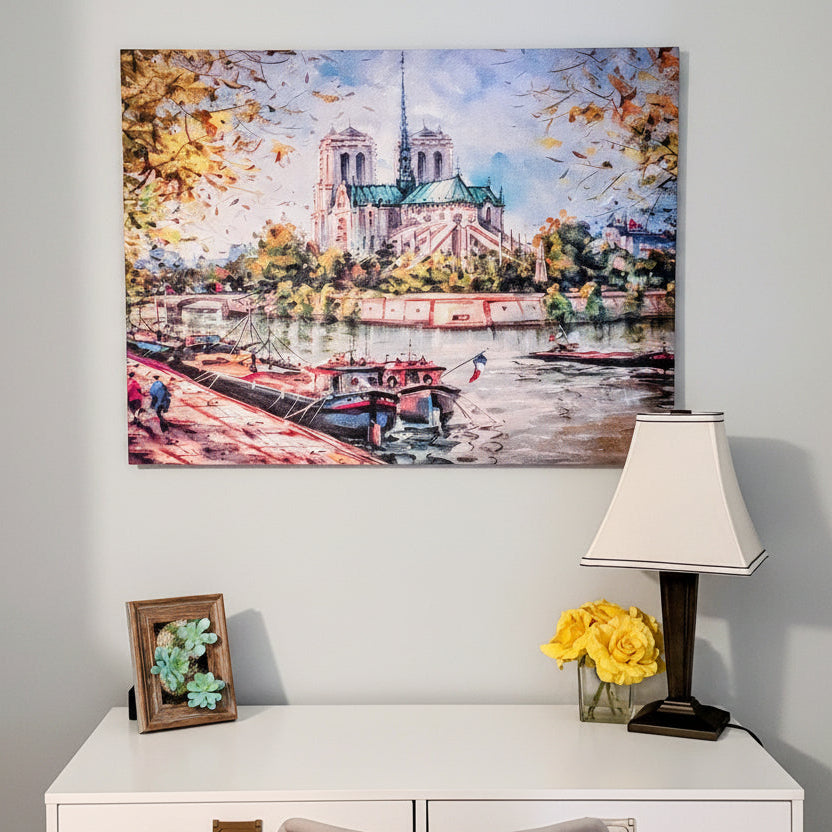 Framed artwork of a cityscape with boats on a river, placed above a white cabinet with a lamp and decorative items.