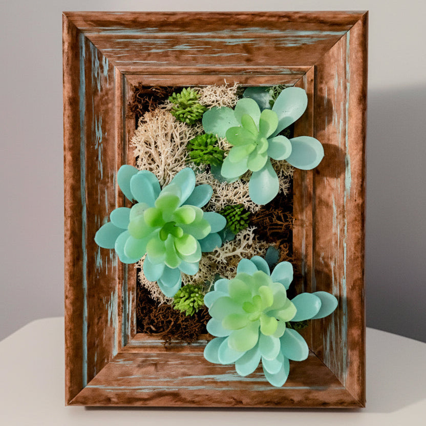 Decorative wall art with succulents and greenery in a wooden frame.