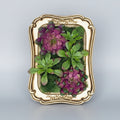 Decorative wall art with green and purple plants in a gold frame on a white background