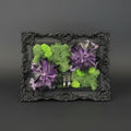 Decorative frame with green and purple artificial flowers on a dark background